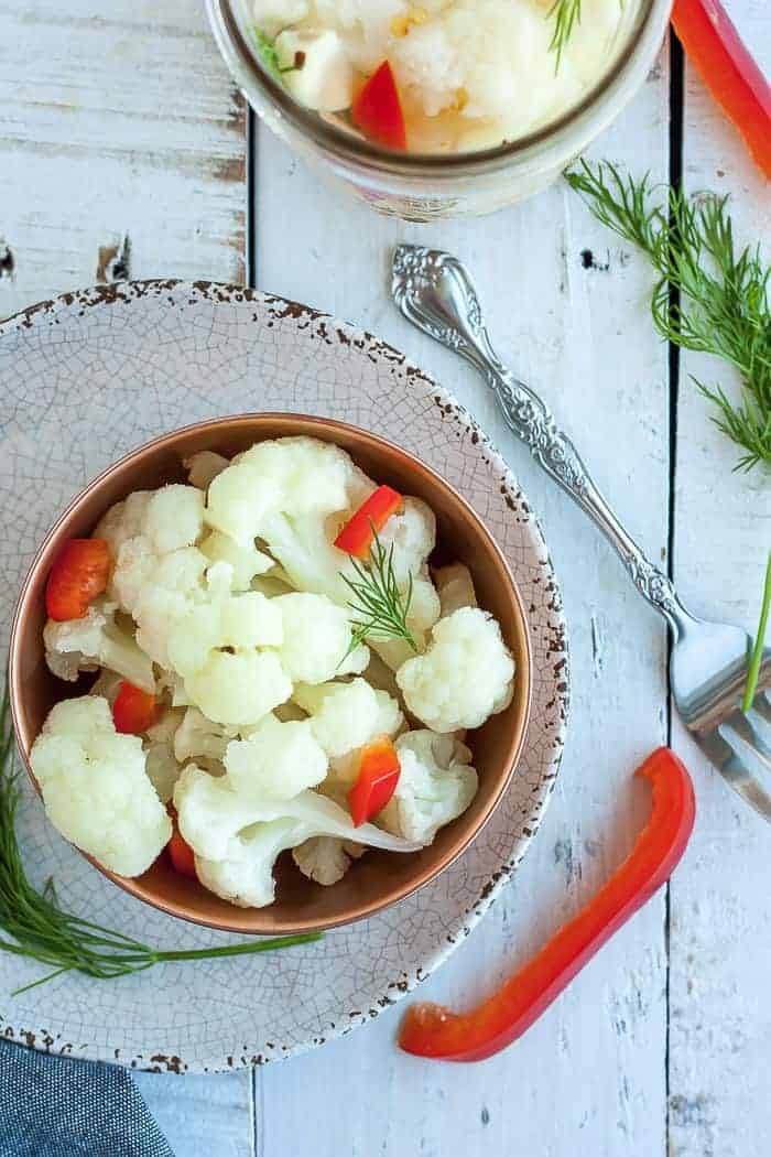 a bowl of pickled cauliflower with red peppers and dill on a white board