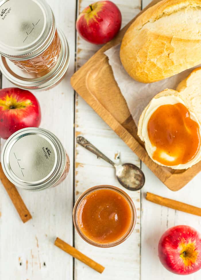 mason jars of apple butter on a white board with buttered french bread