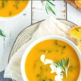 a white bowl of spicy butternut squash soup topped with a white garnish