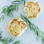 two heads of roasted garlic with fresh herbs on a marble surface