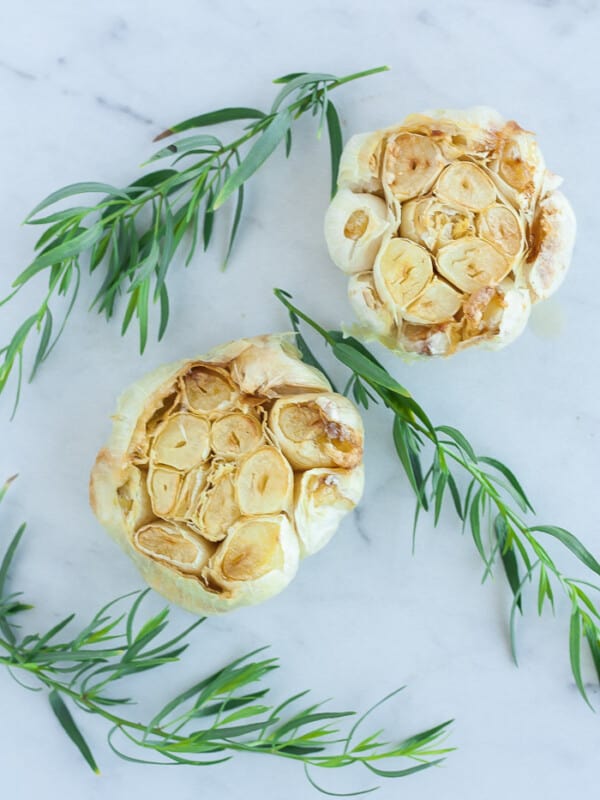 two heads of roasted garlic with fresh herbs on a marble surface