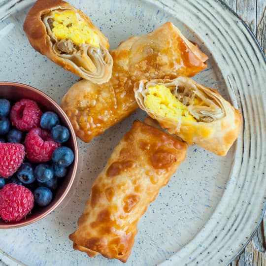 4 bacon and egg rolls and a dish of berries on a grey plate