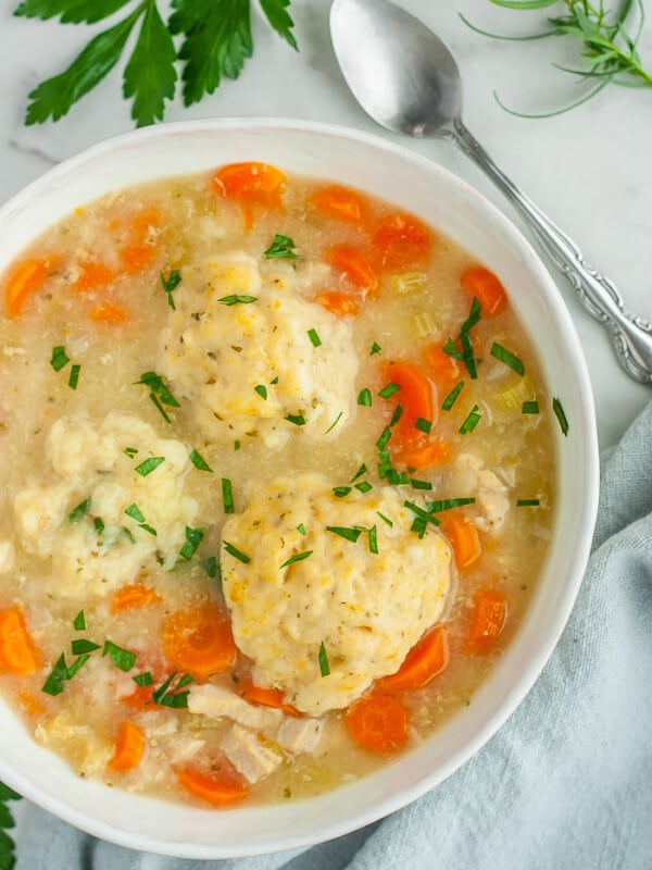 a bowl of instant pot chicken and dumplings with chopped parsley on top and a spoon