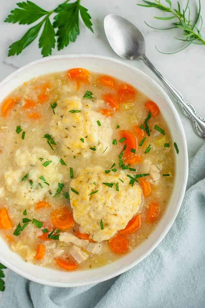 a bowl of instant pot chicken and dumplings with chopped parsley on top and a spoon.