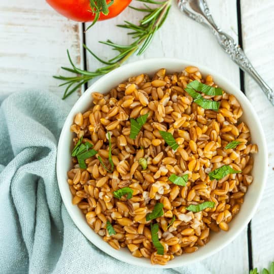 A white bowl with farro topped with chopped parsley