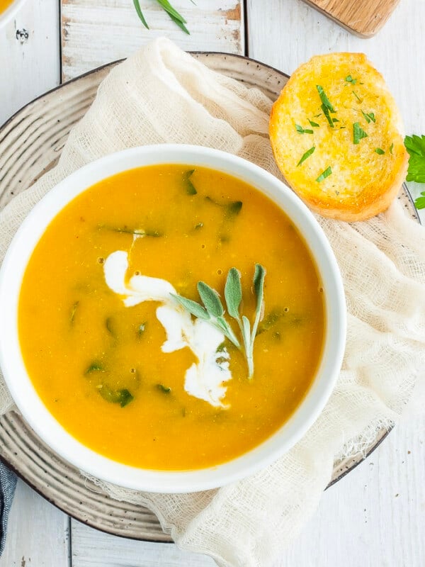 a bowl of vegan butternut squash soup with herbs and bread