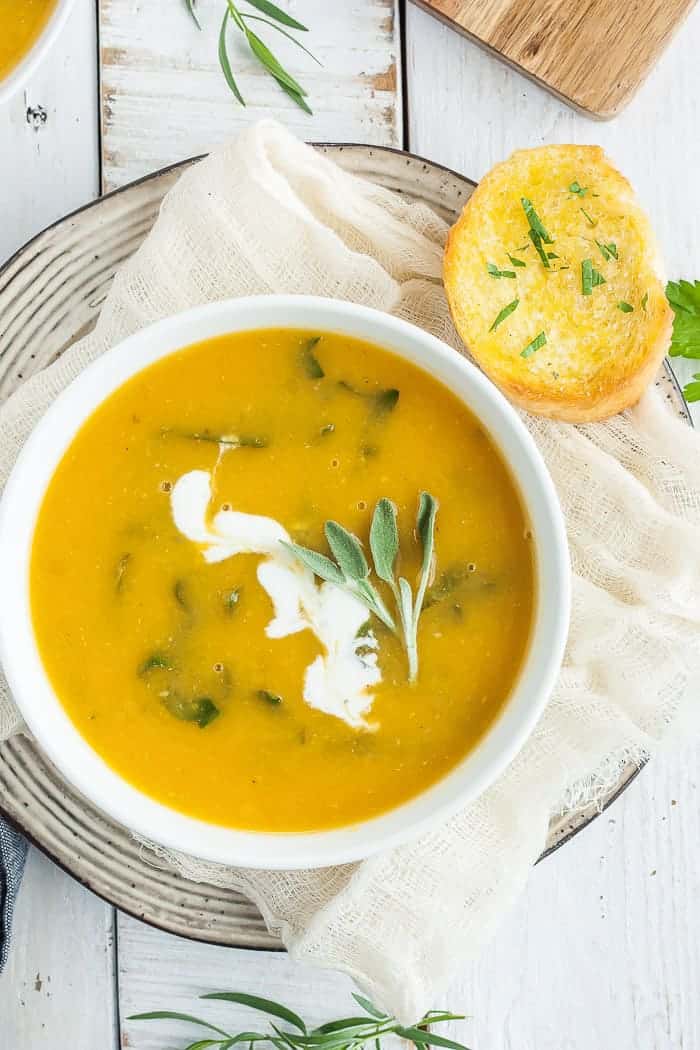 a bowl of vegan butternut squash soup with herbs and bread