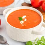 a white bowl of dairy-free tomato soup on a white board with tomatoes and fresh parsley