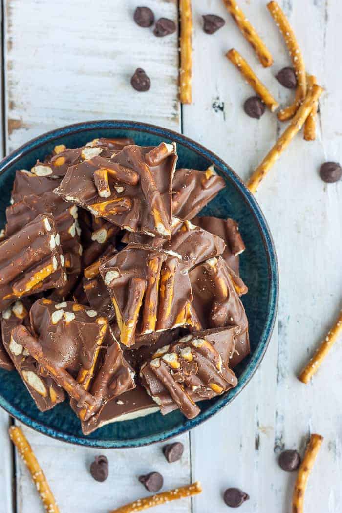 a blue plate with chocolate pretzel bark on a white background with pretzel sticks and chocolate chips