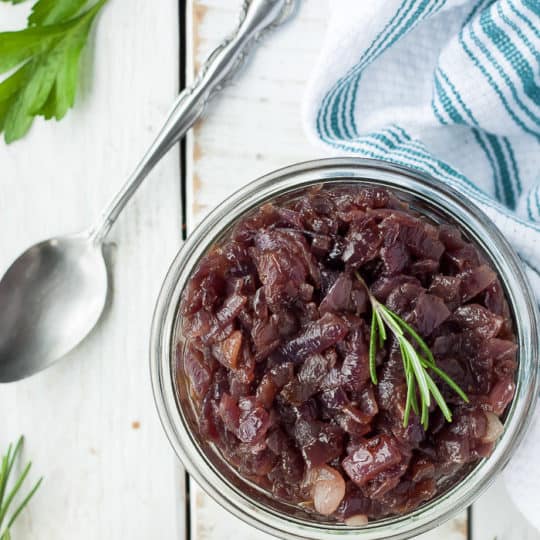 a glass jar of pressure cooker caramelized onions with rosemary and a spoon