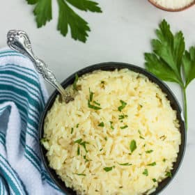 parmesan rice in a blue bowl with parsley, a fork, and white and blue striped cloth