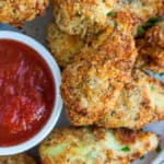 Fried artichoke hearts on a plate with a small bowl of marinara