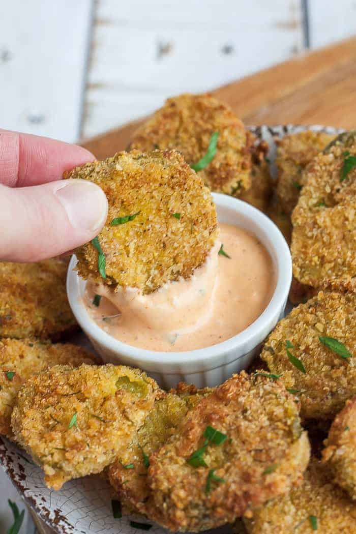 a hand dipping a fried pickle into a bowl of dipping sauce