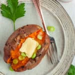 A sweet potato on a tan plate topped with butter and green onions