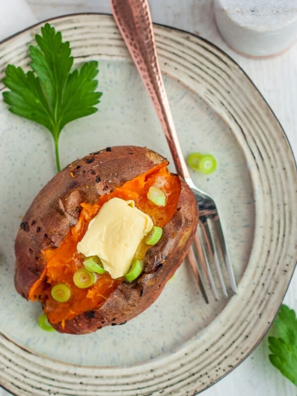 A sweet potato on a tan plate topped with butter and green onions