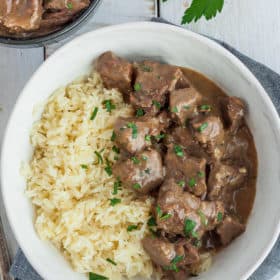 a white bowl with rice and instant pot beef tips and gravy garnished with parsley