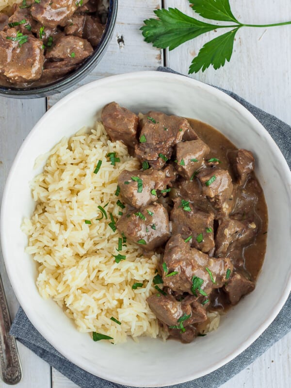 a white bowl with rice and instant pot beef tips and gravy garnished with parsley