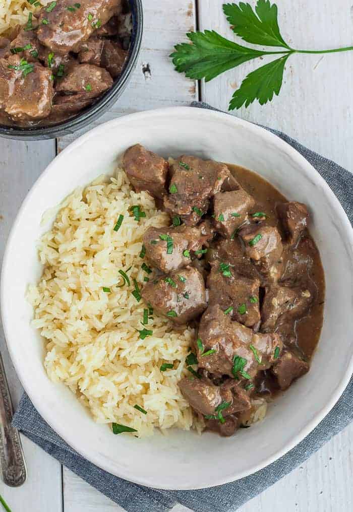 a white bowl with rice and instant pot beef tips and gravy garnished with parsley