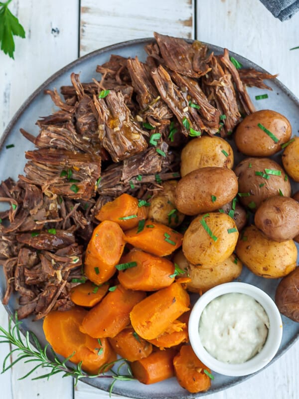 a grey plate with shredded whole30 pot roast, cut carrots, potatoes, and a bowl of horseradish,