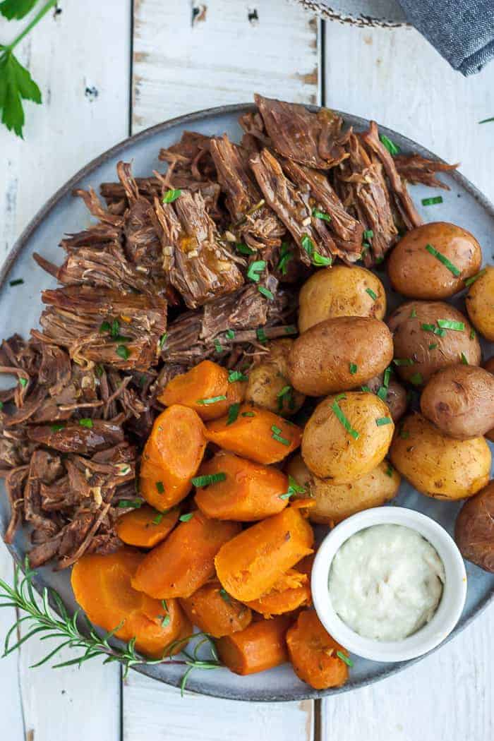 a grey plate with shredded Instant Pot chuck roast, cut carrots, potatoes, and a bowl of horseradish.