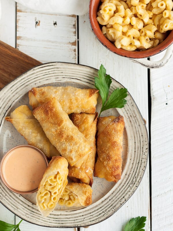 A hand dipping a mac & cheese egg roll into a bowl of buffalo ranch dressing