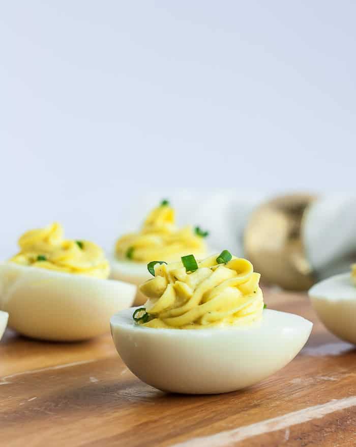 a side profile of greek yogurt deviled eggs on a wooden board, topped with sliced chives.
