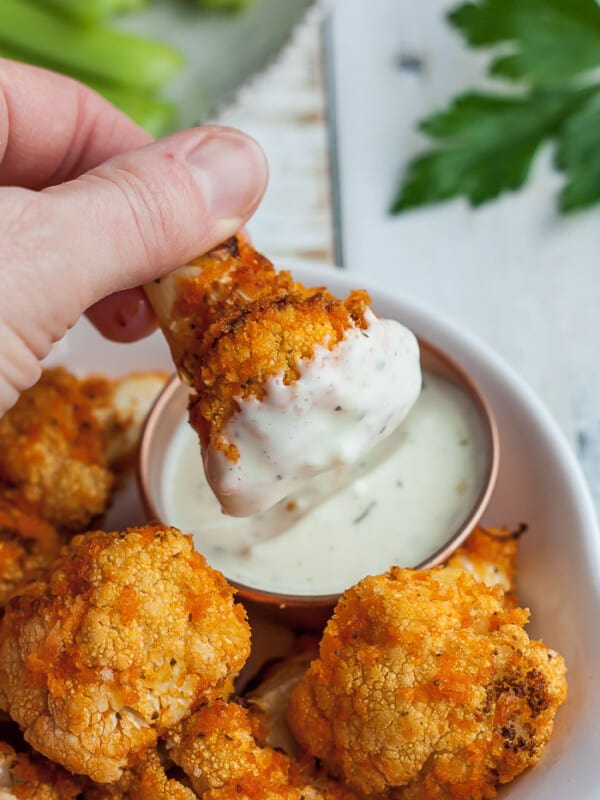 A piece of buffalo cauliflower dipped in a small bowl of ranch dressing