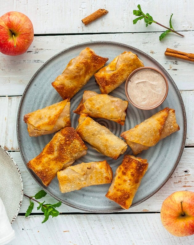 multiple dessert egg rolls on a grey plate with fresh apples and mint.