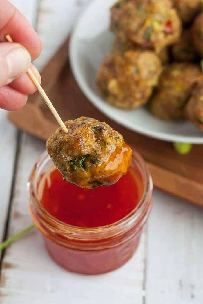 A meatball on a toothpick being dipped into a small bowl of chili sauce