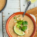 A white and orange bowl of instant pot chicken chili topped with a lime, onions, and cilantro