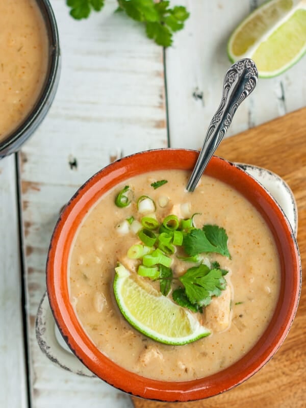 A white and orange bowl of instant pot chicken chili topped with a lime, onions, and cilantro