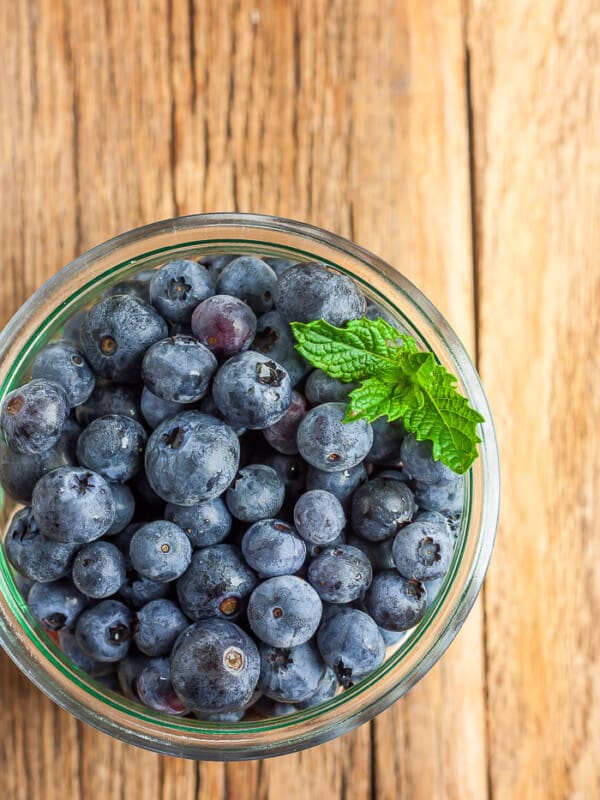 A glass bowl full of blueberries and a sprig of mint on a wooden board
