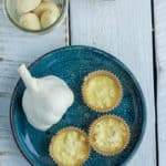 A blue dish with garlic and chopped garlic in muffin liners on a white board