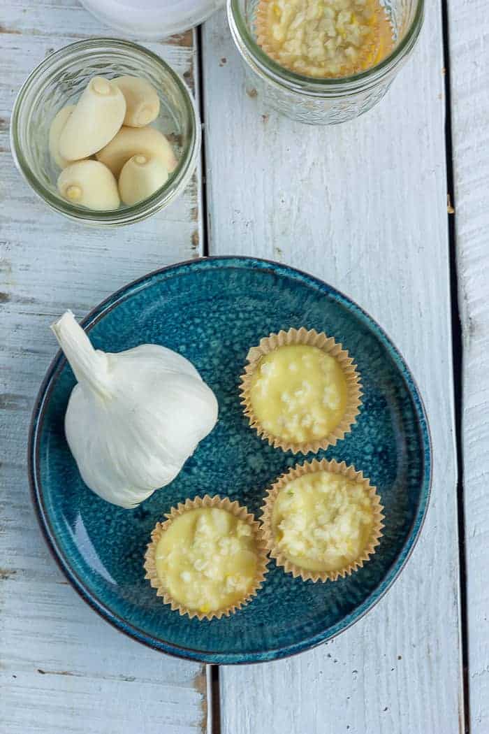 A blue dish with garlic and chopped garlic in muffin liners on a white board
