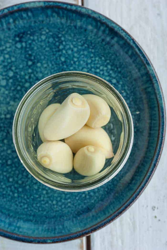 Whole cloves of garlic in a canning jar sitting on a blue plate