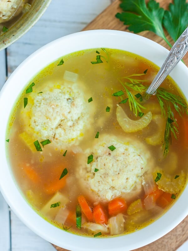A white bowl with matzo ball soup and fresh dill