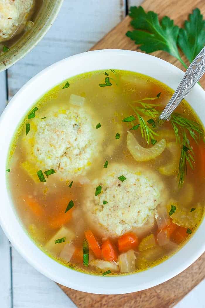 A white bowl with matzo ball soup and fresh dill