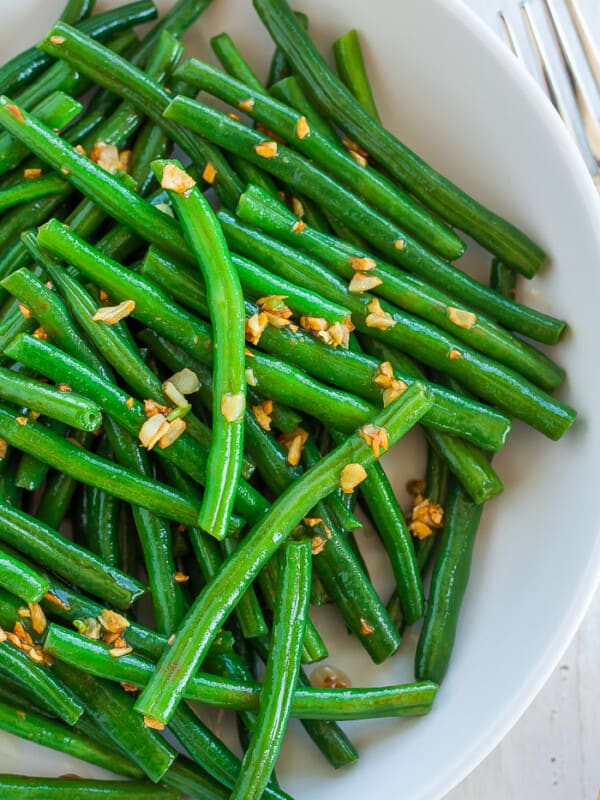 A close up look at a white bowl of green beans topped with garlic