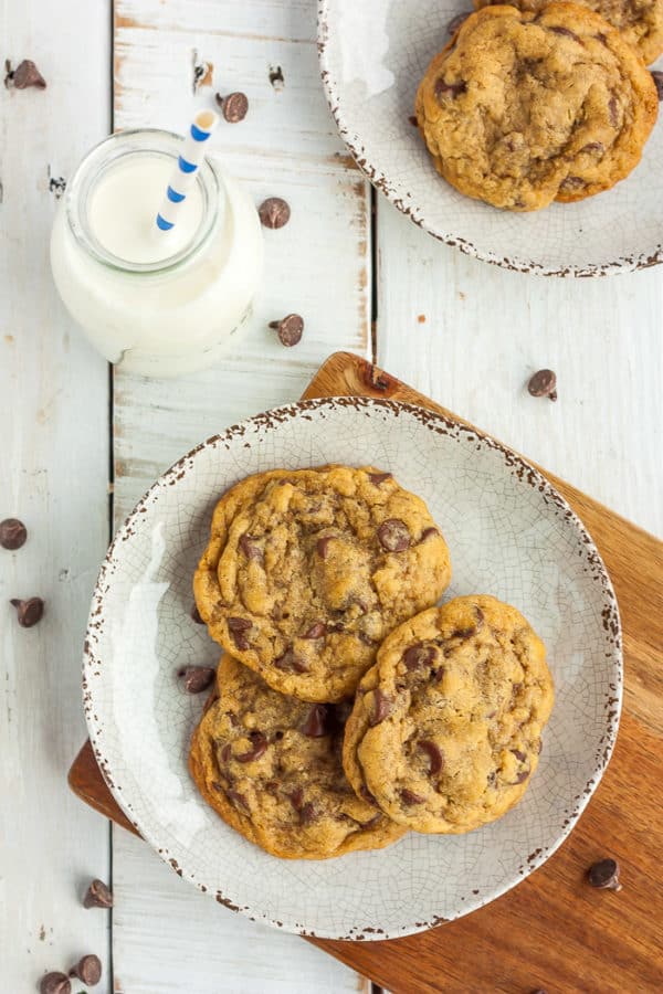 2 plates of chocolate chip cookies on a wooden board with a small bottle of milk that has a straw in it