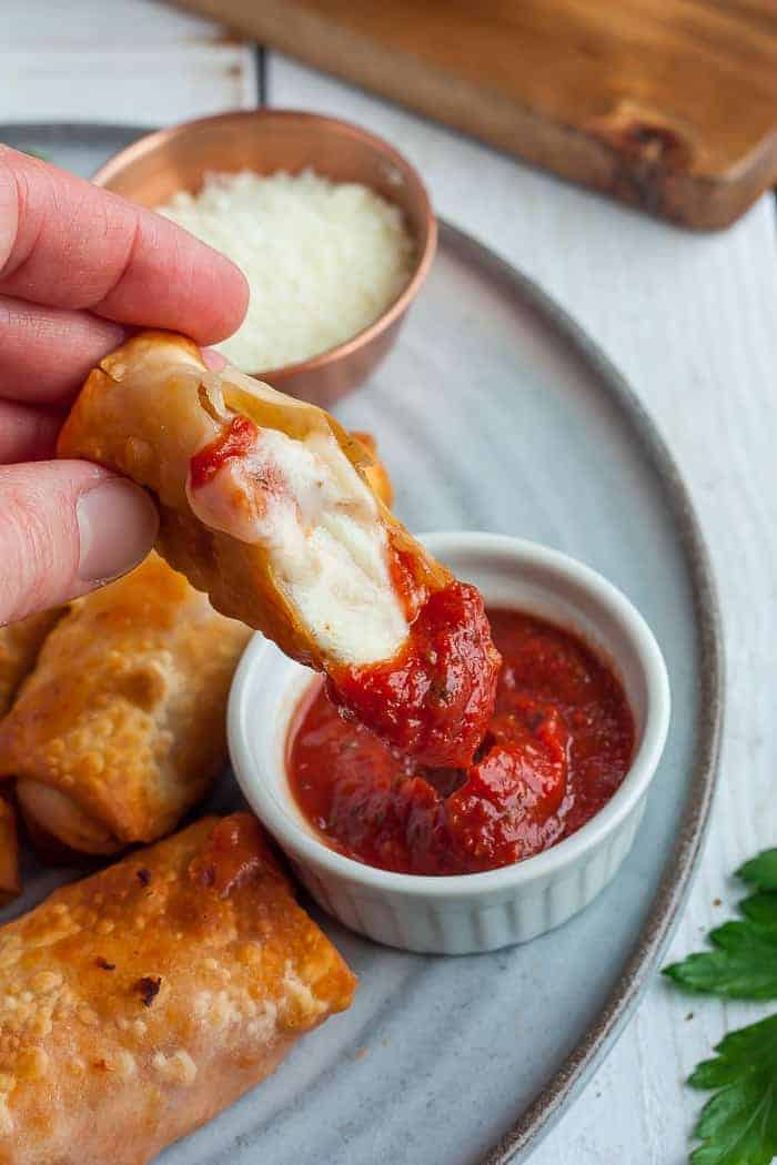 A pizza egg roll being dipped into a small bowl of marinara sauce