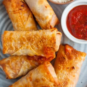 A stack of pizza rolls on a grey plate with a bowl of marinara and a bowl of parmesan cheese