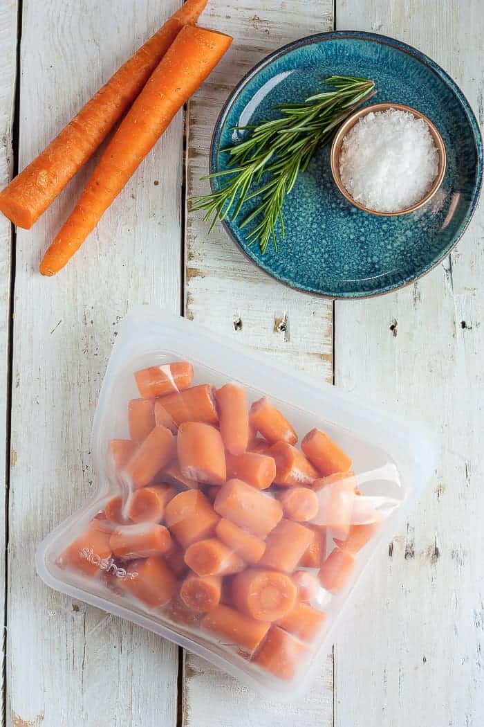 A freezer bag of frozen carrots and a blue dish with herbs and a bowl of salt
