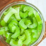 A round glass bowl full of chopped frozen celery on a wooden cutting board