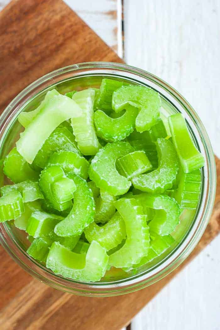 A round glass bowl full of chopped frozen celery on a wooden cutting board