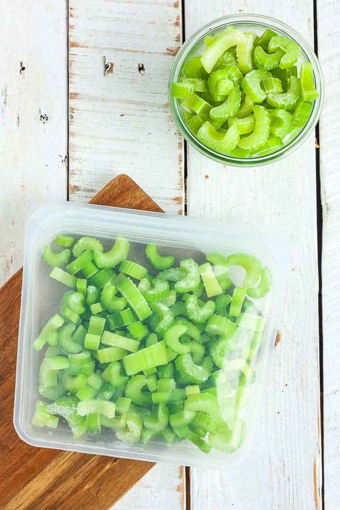 a silicone bag of sliced frozen celery on a wooden board and a small glass bowl with celery
