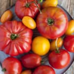 Multiple kinds of tomatoes on a grey plate on a wooden board