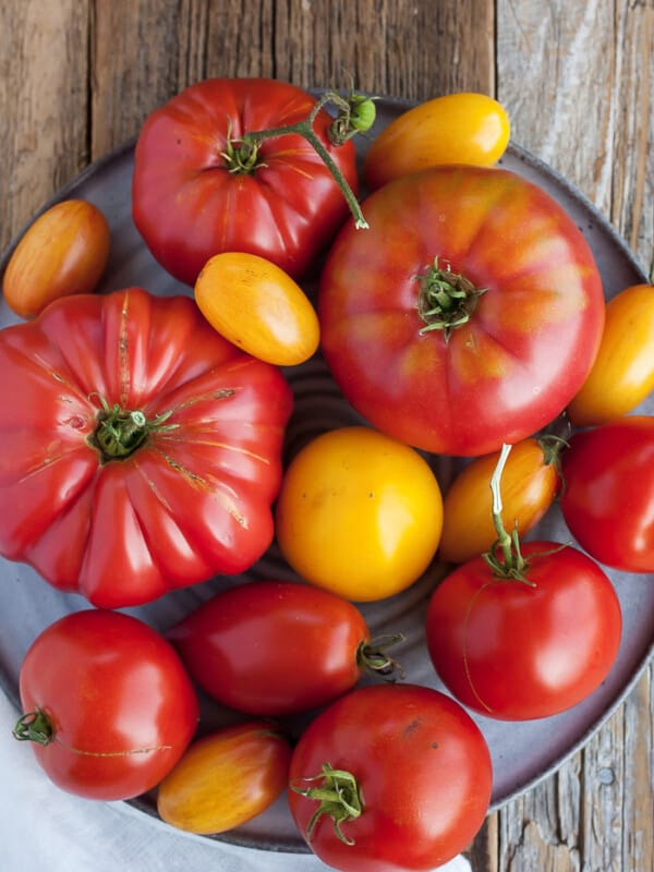 Multiple kinds of tomatoes on a grey plate on a wooden board