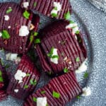 A grey plate with roasted beets topped with goat cheese, hazelbuts, and parsley