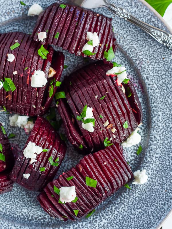 A grey plate with roasted beets topped with goat cheese, hazelbuts, and parsley