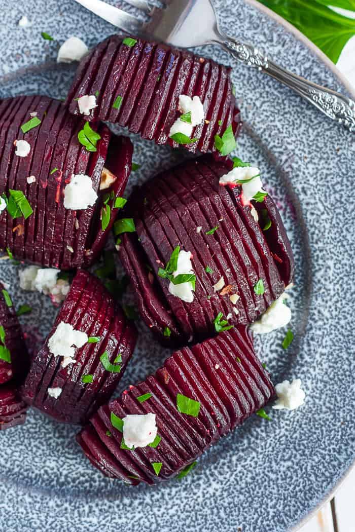 A grey plate with roasted beets topped with goat cheese, hazelbuts, and parsley